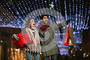 Couple in the city centre with holiday`s brights in background. Couple holding gift in a Christmas night