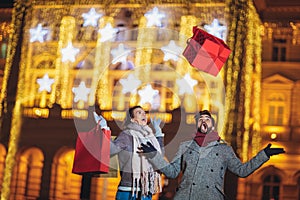 Couple in the city centre with holiday`s brights in background. Man presenting gift to woman, having fun