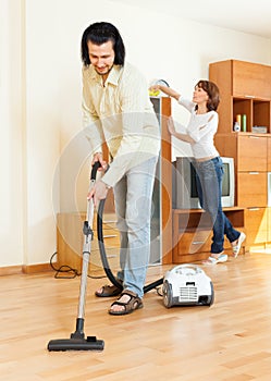 Couple cleaning with vacuum cleaner in home