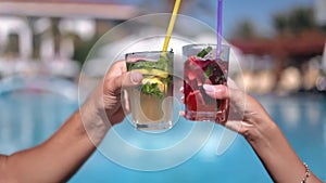 Couple clinking glasses cheers summer cocktails with straw sunbathing swimming pool luxury resort