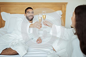 Couple Clinking Glasses Drinking Sparkling Wine Wearing Bathrobes In Hotel