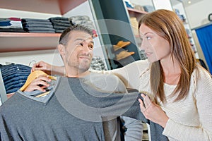 Couple in clothes shop lady holding jumper against man