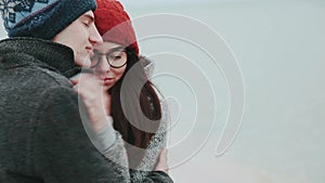 Couple on the coast of the sea, in a winter coat and a girl in a red cap and glasses.