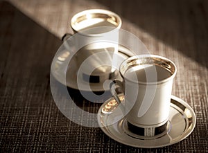 A couple of coffee cups on a brown table in the sunlight. Selective focus