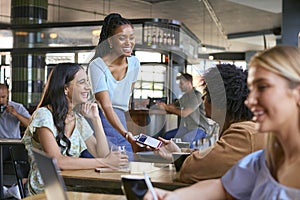 Couple In Coffee Shop Meeting With Man Paying Bill With Contactless Mobile Phone Payment