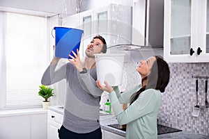 Couple Collecting Water Leaking From Ceiling In Bucket