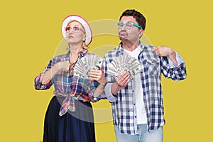 Couple of confident friends, adult man and woman in casual checkered shirt standing together holding fan of dollars and pointing