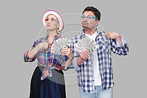 Couple of confident friends, adult man and woman in casual checkered shirt standing together holding fan of dollars and pointing