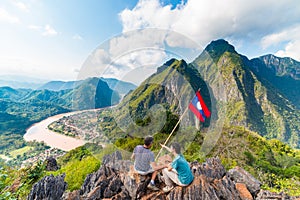 Couple conquering mountain top at Nong Khiaw panoramic view over Nam Ou River valley Laos national flag scenic mountain landscape