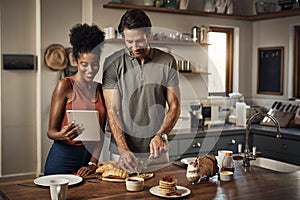 Couple cooking breakfast with a tablet while searching for online recipes and videos on the internet. Happy interracial