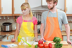 Couple cooking in kitchen reading cookbook