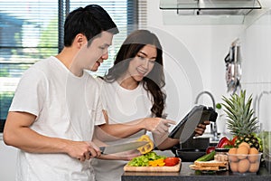 Couple cooking and preparing vegetables according to a recipe on a tablet computer in kitchen at home