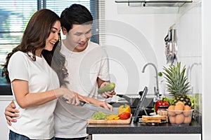 Couple cooking and preparing vegetables according to a recipe on a tablet computer in kitchen at home