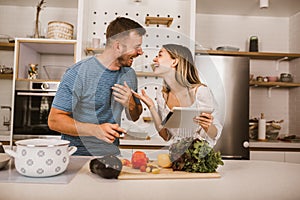 Couple cooking together in kitchen reading recipes on digital tablet