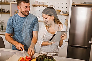 Couple cooking together in kitchen reading recipes on digital tablet