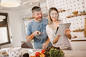 Couple cooking together in kitchen reading recipes on digital tablet