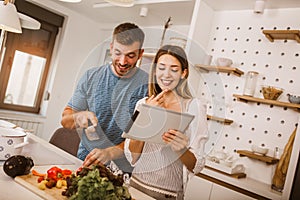 Couple cooking together in kitchen reading recipes on digital tablet