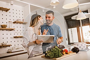 Couple cooking together in kitchen reading recipes on digital tablet