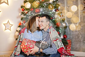 Couple couple in love under a blanket near the Christmas tree give each other gifts