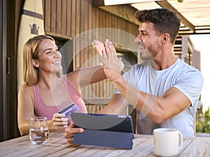 Couple With Credit Card Using Digital Tablet At Home To Book Holiday Or Shop Online Giving High Five