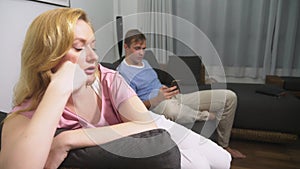 Couple crisis. Man and woman spend the evening in the living room on the couch. the man uses the phone, the woman is