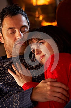 Couple Cuddling On Sofa By Cosy Log Fire