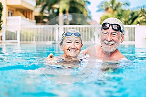 Couple of cute seniors and pensioners in the water of the pool having fun and enjoying together - two mature people in love