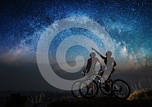 Couple cyclists with mountain bikes at night under starry sky