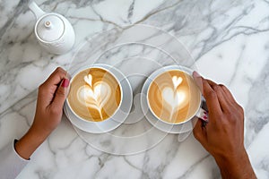 Couple on a date, man and woman hands holding coffee cup with latte art. Cappuccino crema of heart shape. Top view of marble cafe