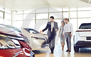 Couple and the dealer selling cars look the car in the showroom.