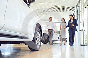 Couple and the dealer selling cars look the car in the showroom.