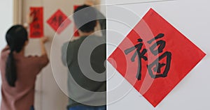 Couple decorating red chinese calligraphy stick on the door at home, word mean luck