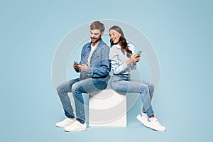 Couple in denim on cube using phones, back-to-back