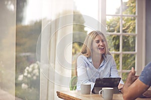 Couple With Digital Tablet Sitting At Table Working From Home Viewd Through Window