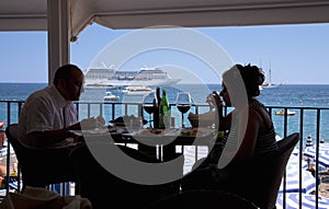 Couple dining in foreground with cruise ship in background at Amalfi, a town in the province of Salerno, in the region of