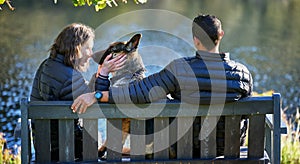 Couple, dog and back on park bench, outdoor and relax by lake for connection, care or touch on holiday. Man, woman and