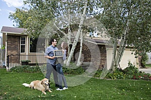 Couple and dog family in front of new home holding sold blackboard sign and keys