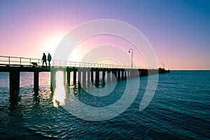 Couple with dog silhouettes on wooden pier at sunset.