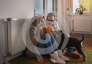 Couple with dog sitting beside radiator and freezing