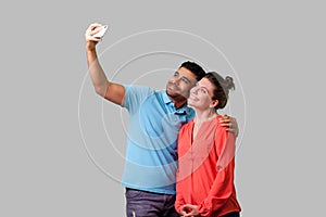 Couple doing selfie! Portrait of positive young man and woman in casual wear taking pictures. isolated on gray background, indoor