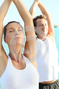 Couple doing yoga by the sea