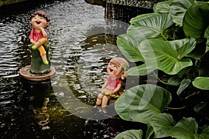 Couple dolls made of clay in pond at small garden.