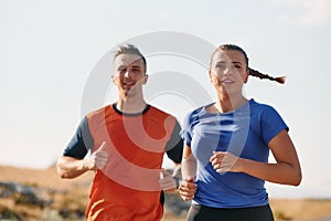 A couple dressed in sportswear runs along a scenic road during an early morning workout, enjoying the fresh air and