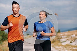 A couple dressed in sportswear runs along a scenic road during an early morning workout, enjoying the fresh air and