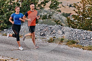 A couple dressed in sportswear runs along a scenic road during an early morning workout, enjoying the fresh air and