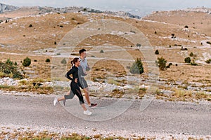 A couple dressed in sportswear runs along a scenic road during an early morning workout, enjoying the fresh air and
