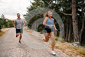 A couple dressed in sportswear runs along a scenic road during an early morning workout, enjoying the fresh air and