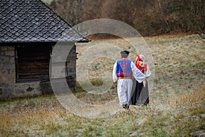 Pár oblečený v tradičním lidovém kroji. Slovenský kroj v podzimní přírodě. Stará venkovská chalupa v pozadí. Mladý pár