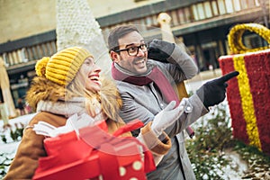 Couple dressed in winter clothing holding gift boxes outdoor. Selective focus