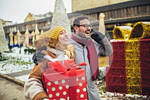 Couple dressed in winter clothing holding gift boxes outdoor. Selective focus